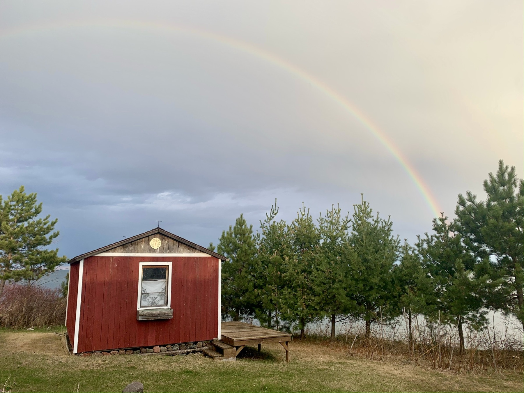 A rainbow above a red shed and pine trees in northern Minnesota.